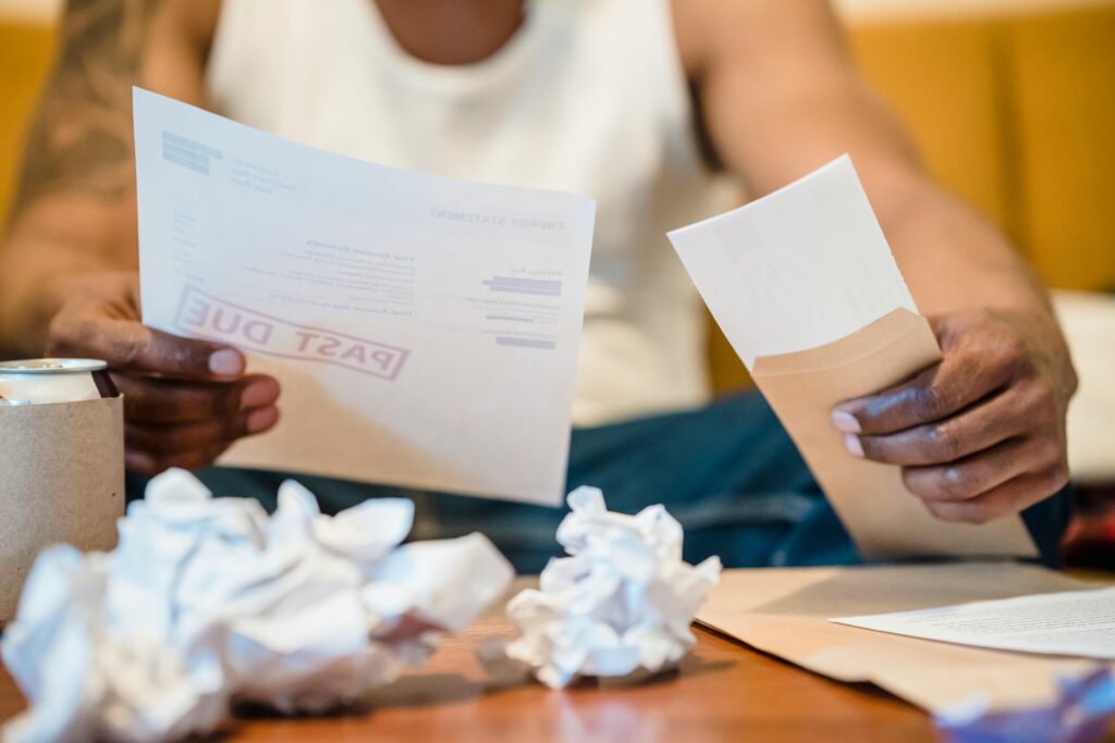 A working American adult sits at a kitchen table reviewing bills and financial documents, representing the $3,800 per-household cost increase caused by Liberation Day tariff policies in 2025 and 2026