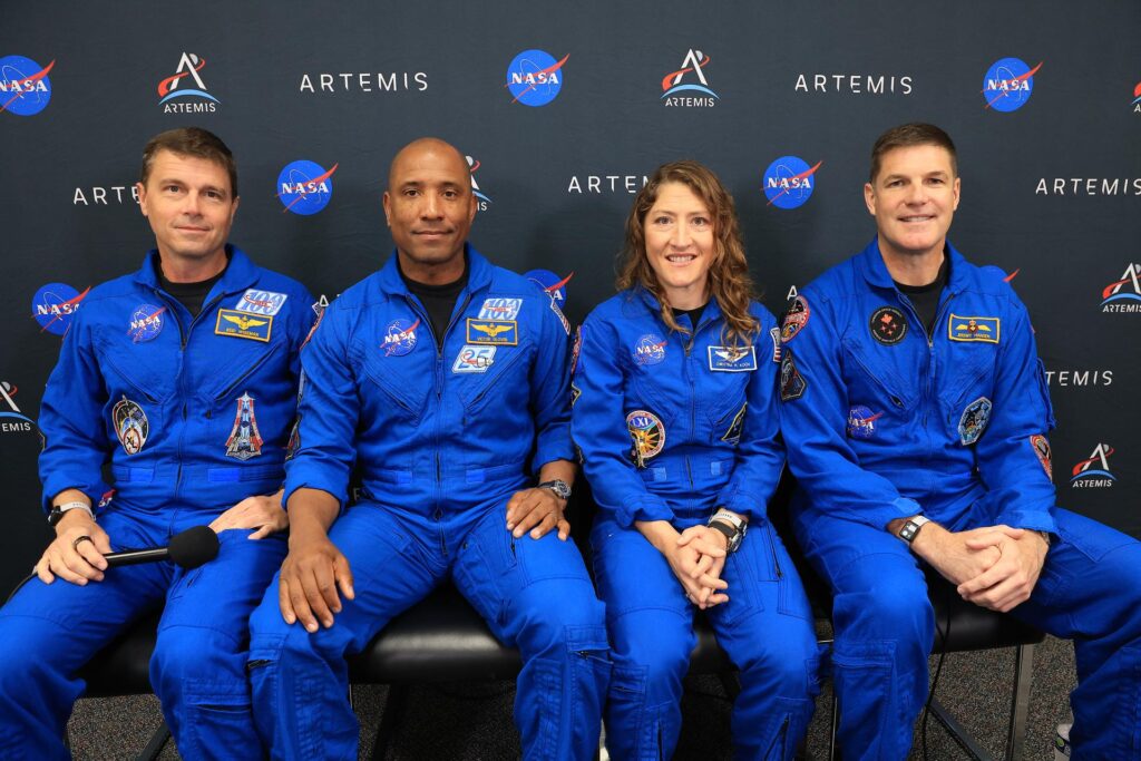 Artemis II crew members Jeremy Hansen, Victor Glover, Reid Wiseman, and Christina Koch pose in orange Orion spacesuits at NASA's Kennedy Space Center