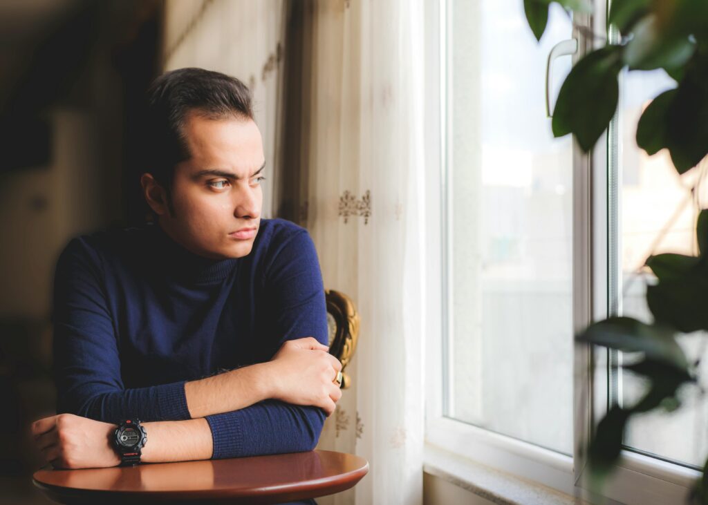 A thoughtful American adult looking out a window, representing resilience and the struggle of affording life on a $60,000 salary in 2026